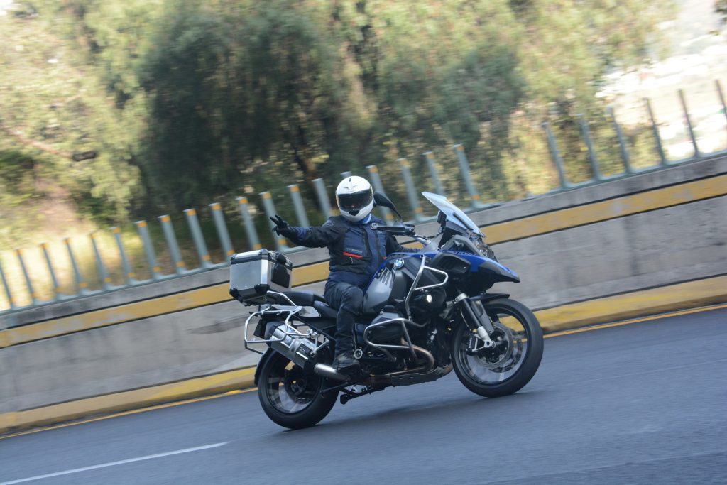 Motard sur un BWM 1200GS qui roule et fait le signe motard "V" avec les doigts