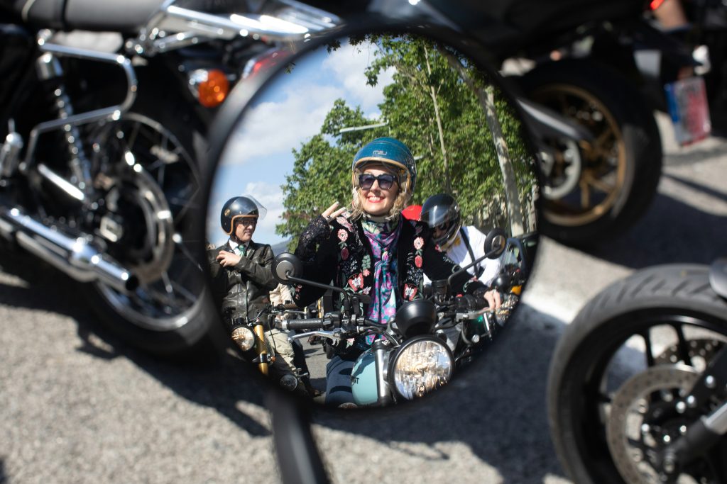 Vue de rétroviseur, une femme sourit et fait le signe motard "V"
